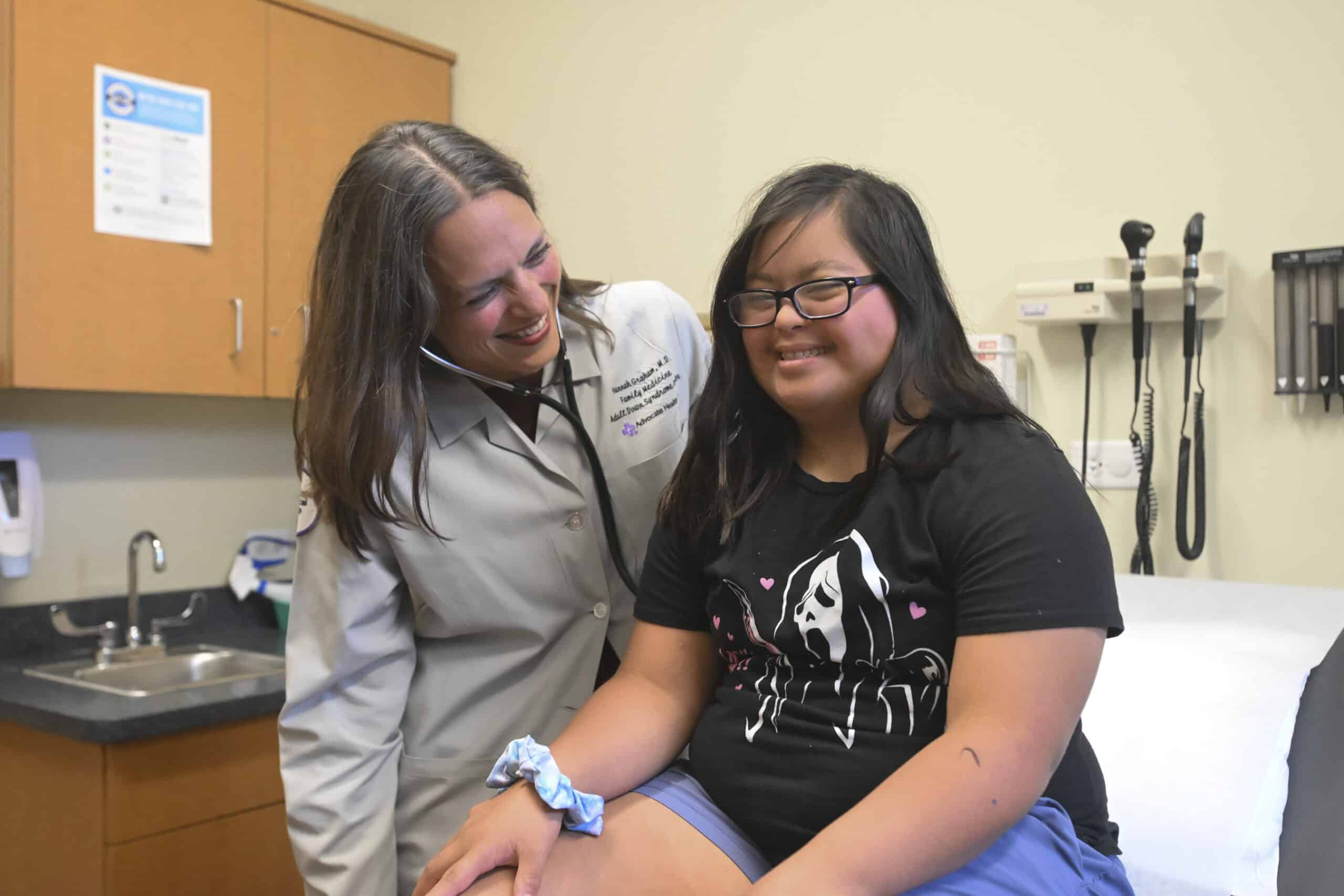 Female doctor standing next to a young woman with Down syndrome sitting on an exam table