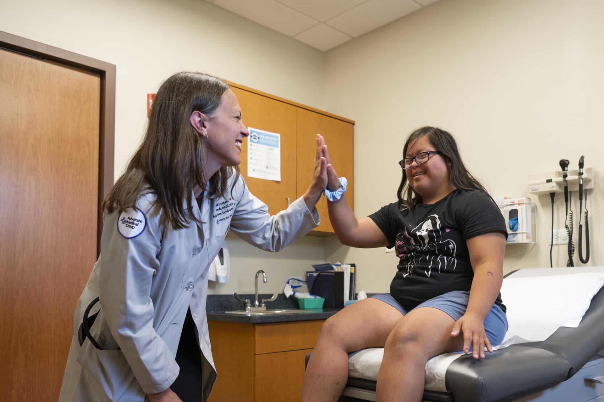 Female doctor and female patient with Down syndrome giving each other a high five.